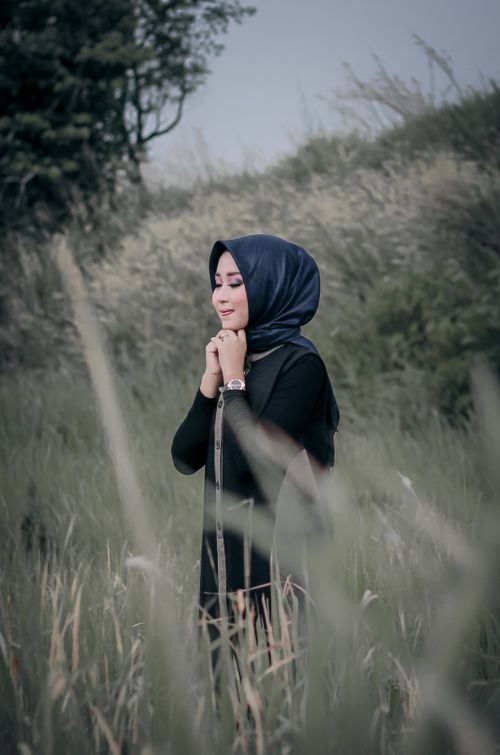 Free A serene portrait of a woman in traditional wear standing in a lush grass field, enjoying solitude. Stock Photo