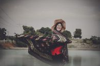 一位戴着帽子和披肩的快乐女子，在户外湖边微笑着