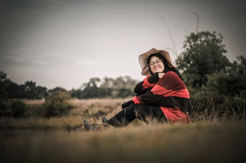 Woman Sitting on Grass Wearing Red-and-black Long-sleeved Shirt and Black Pants