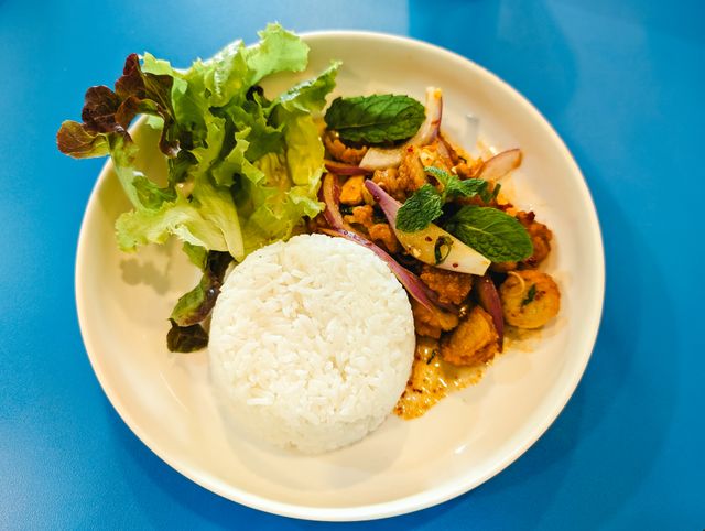A vibrant Thai meal featuring rice, fresh greens, and flavorful chicken set on a blue background.