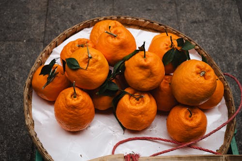 A basket of oranges on a table with leaves