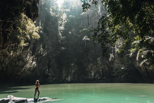 Free A woman stands on a rock near a clear waterfall surrounded by lush greenery. Stock Photo