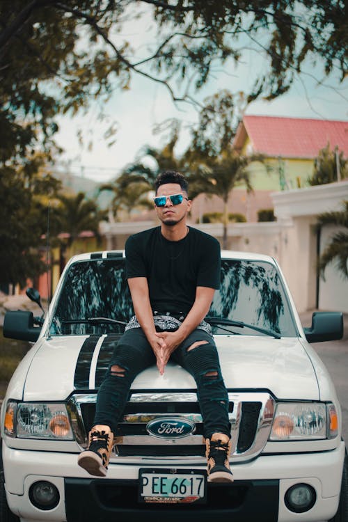 Man Wearing Black T-Shirt Sitting on White Ford Car Hood