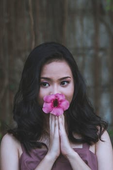 一个女人在户外，手拿粉红色的芙蓉花遮在脸前