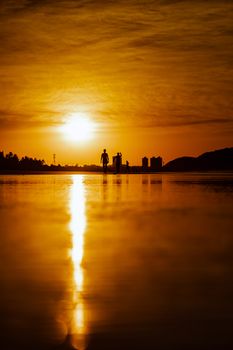 Silhouette of people walking along a beach during a dramatic sunset with vivid reflections on the water.