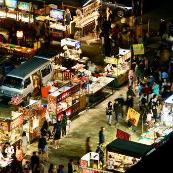 High-angle view of a bustling night market filled with colorful food stalls and lively crowds.