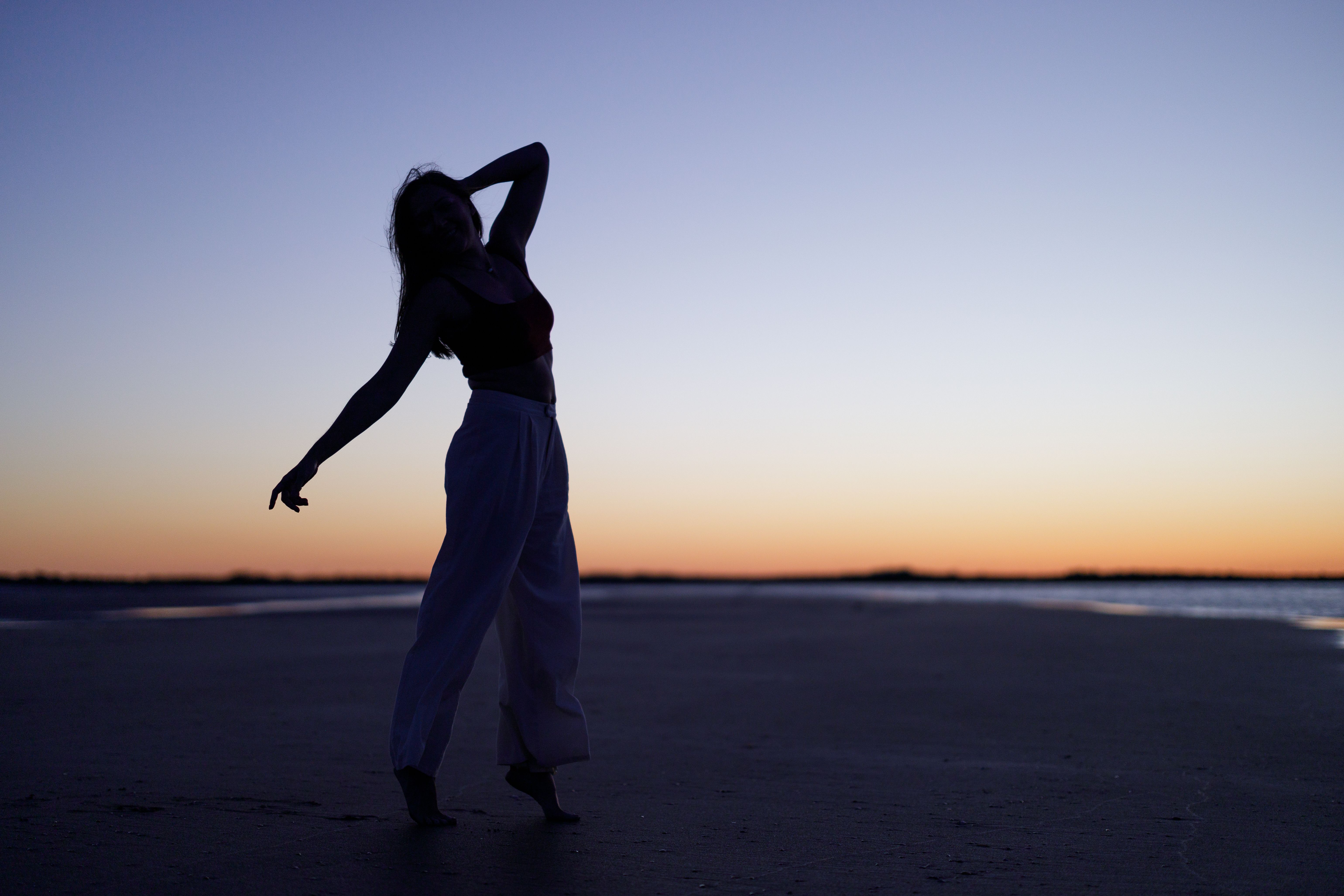 Silhouette of a Woman Standing on a Beach at Sunset · Free Stock Photo