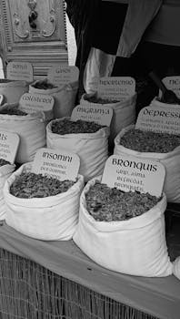 Black and white photo of herbs and spices at a market stall, focusing on alternative medicine.