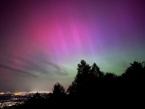 Vibrant aurora borealis and city lights under a clear night sky.