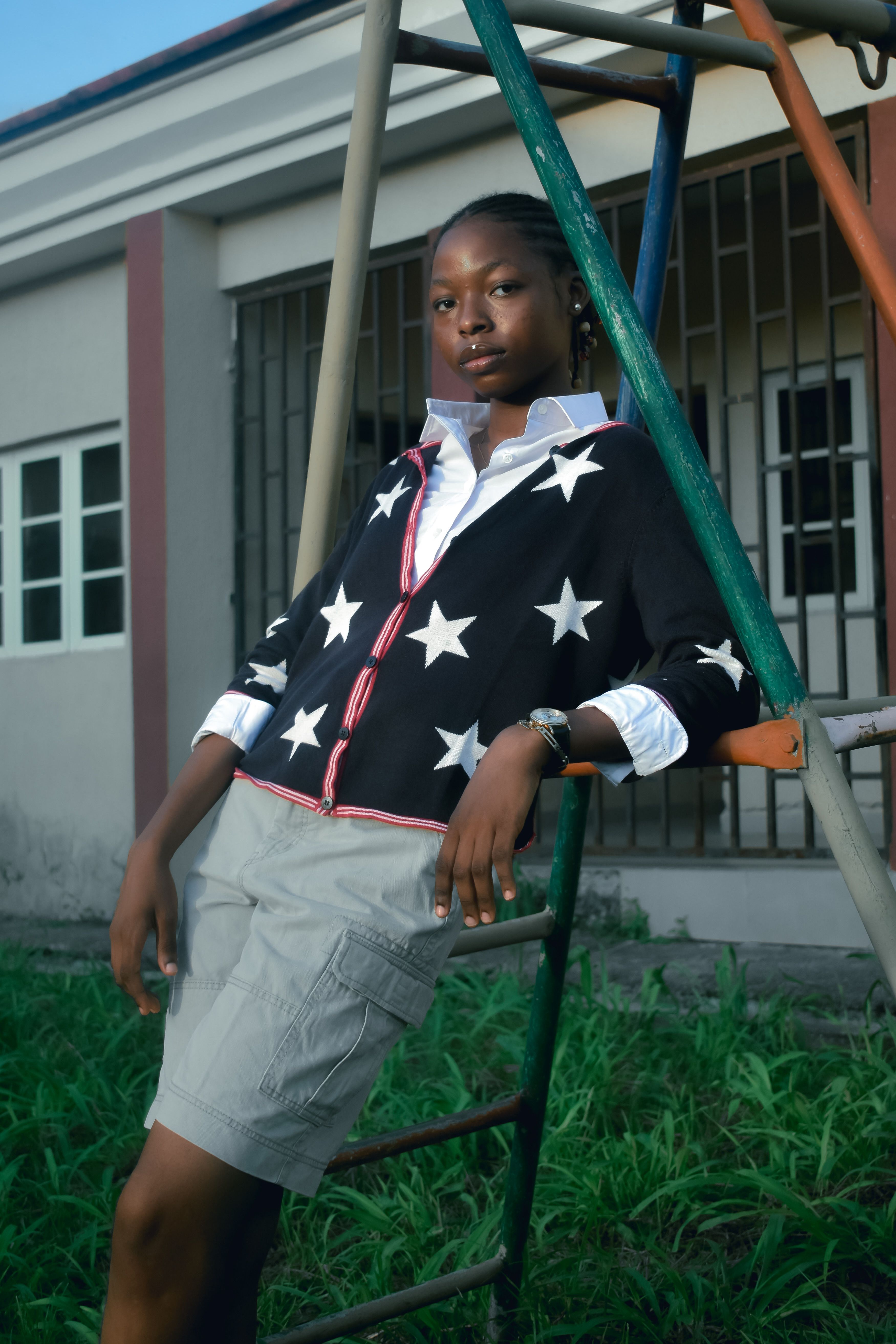 Confident woman leaning on playground equipment wearing a star-patterned sweater and shorts.