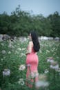 A pregnant woman in a pink dress stands in a field of flowers