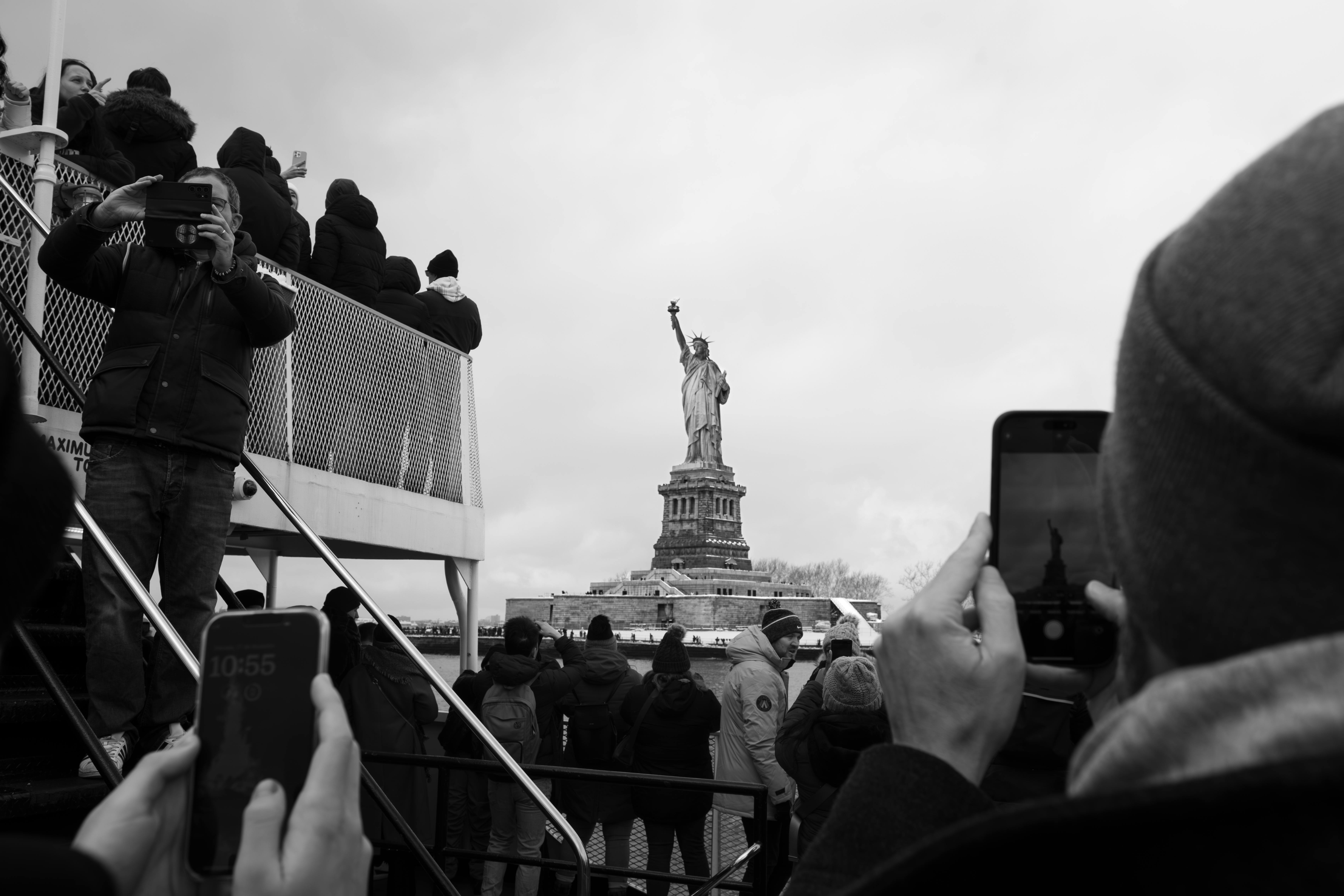 Black and white photo of tourists taking pictures of the Statue of Liberty from a New York City ferry.