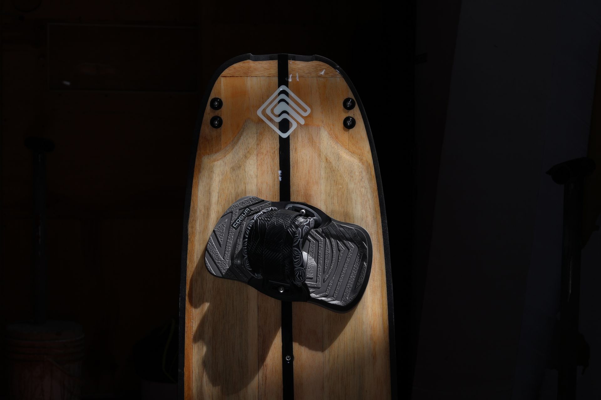 Detailed view of a wooden wakeboard with attached binding in a studio setting.