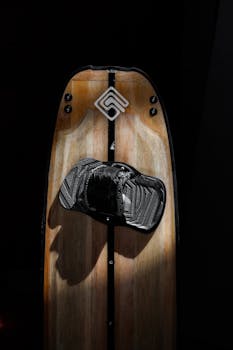 Vertical shot of a wooden wakeboard with black binding against a black studio background.