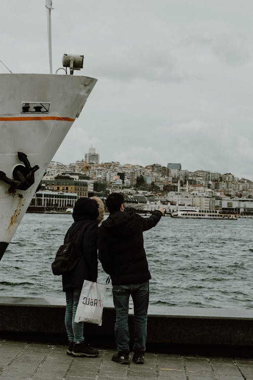 Two people standing near a boat and looking at the water