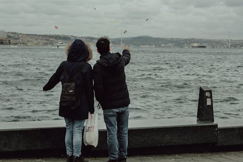 A couple standing on a pier looking at a kite