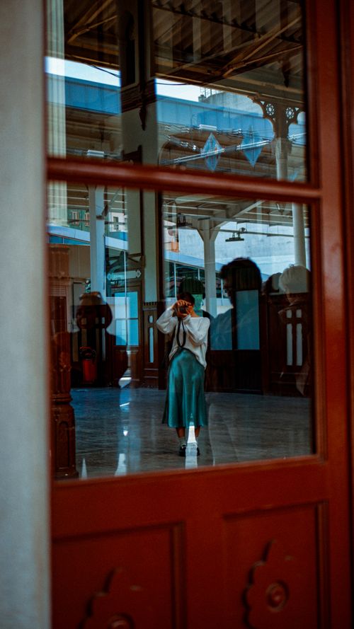 Free A woman photographs herself through a vintage glass door reflection in an elegant hall. Stock Photo
