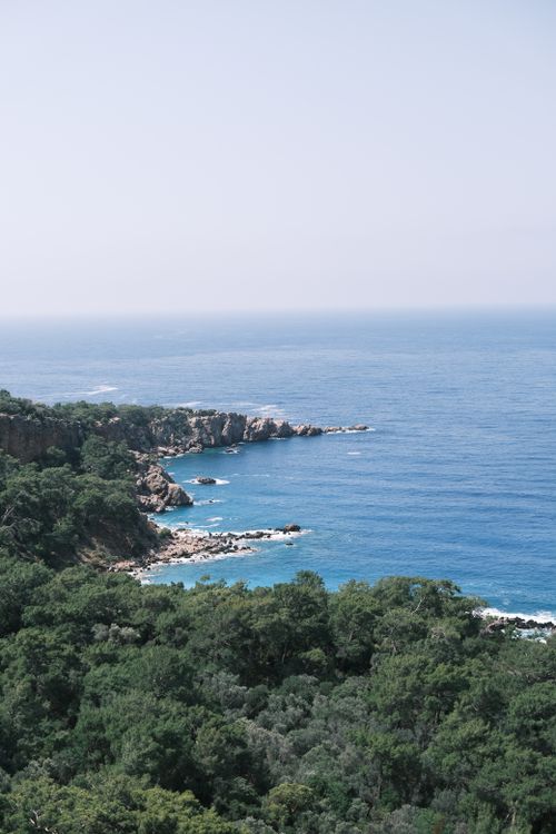 Free A breathtaking view of a rocky coastline with a lush forest and calm blue sea under a clear sky. Stock Photo