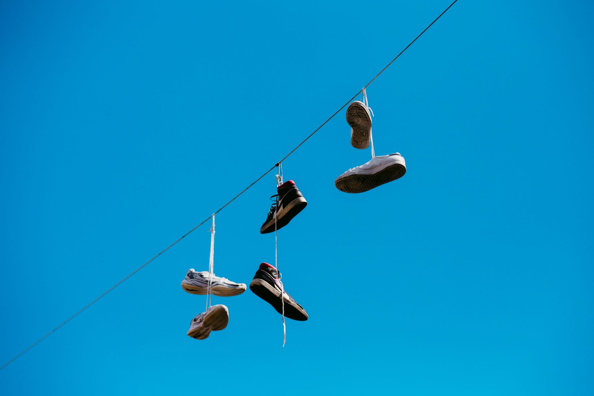 Shoes hanging on a line under a clear blue sky in Rimini, Italy.