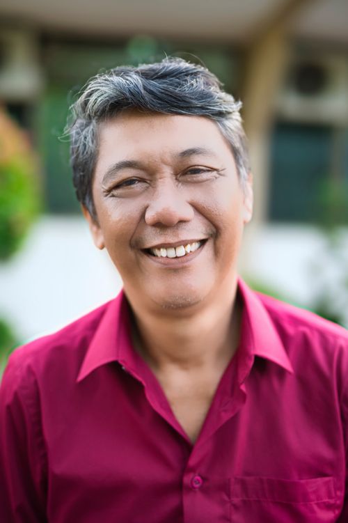 Free Portrait of a cheerful middle-aged man smiling warmly in a red shirt outdoors during the day. Stock Photo