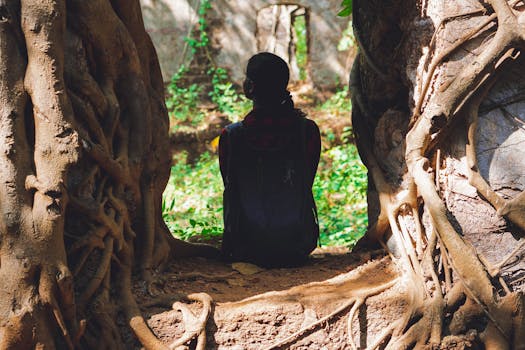 A person sits among large entwined tree roots, capturing a serene moment in nature.