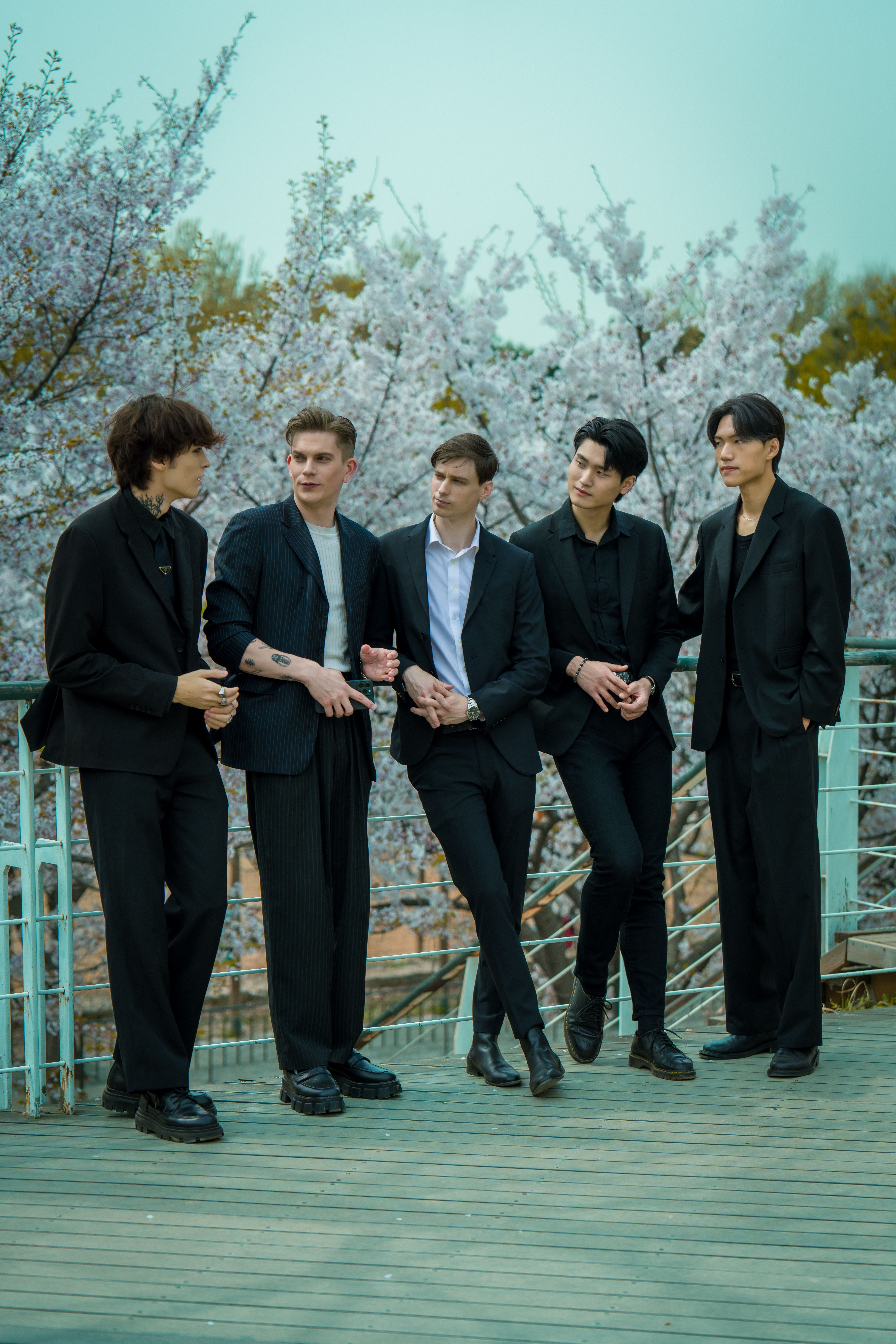 Group of young men in black suits standing on a terrace in Seoul, with cherry blossoms.