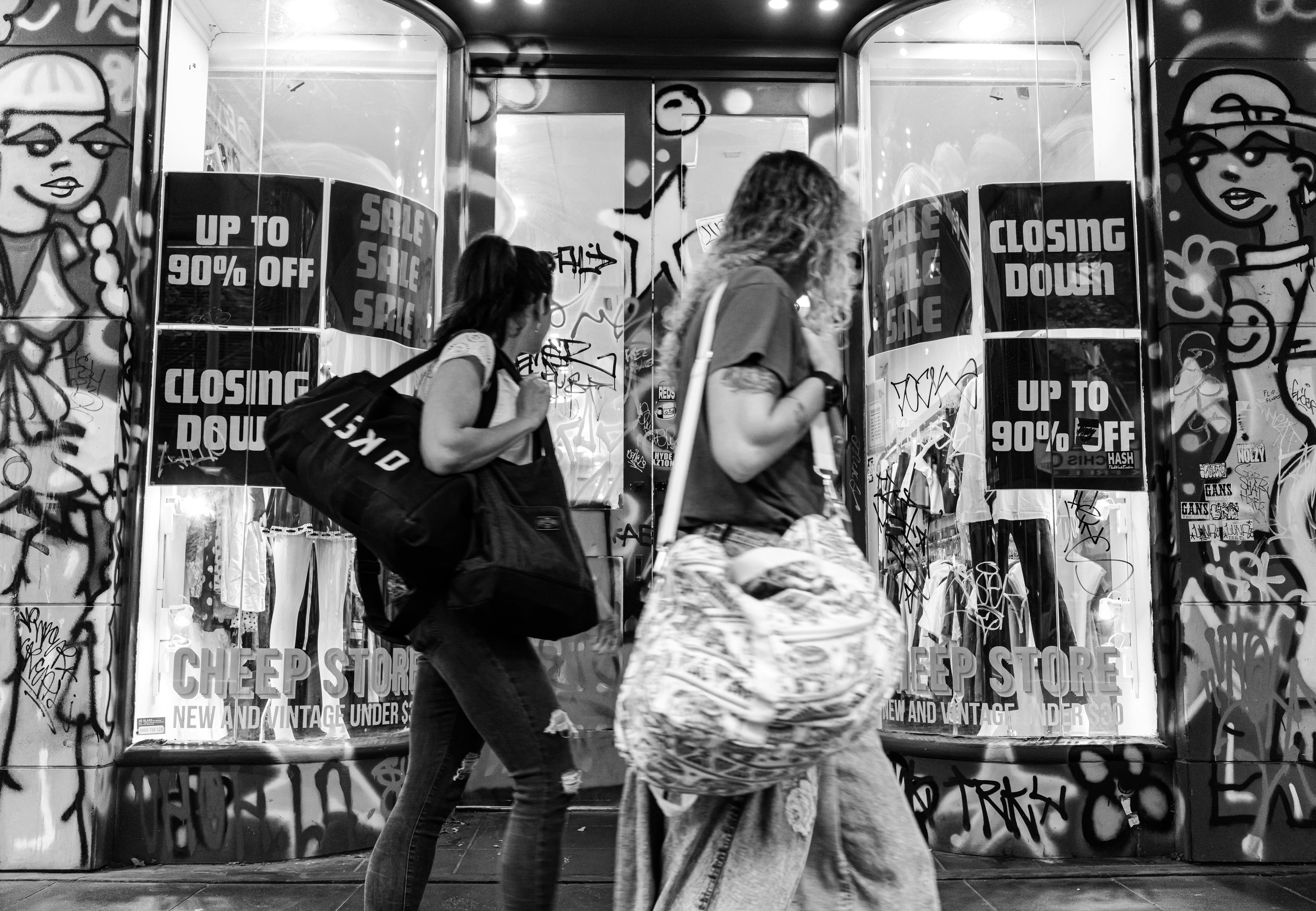 Black and white photo of pedestrians passing by a closing store in Melbourne with graffiti art.
