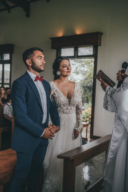 A bride and groom are standing in front of a priest