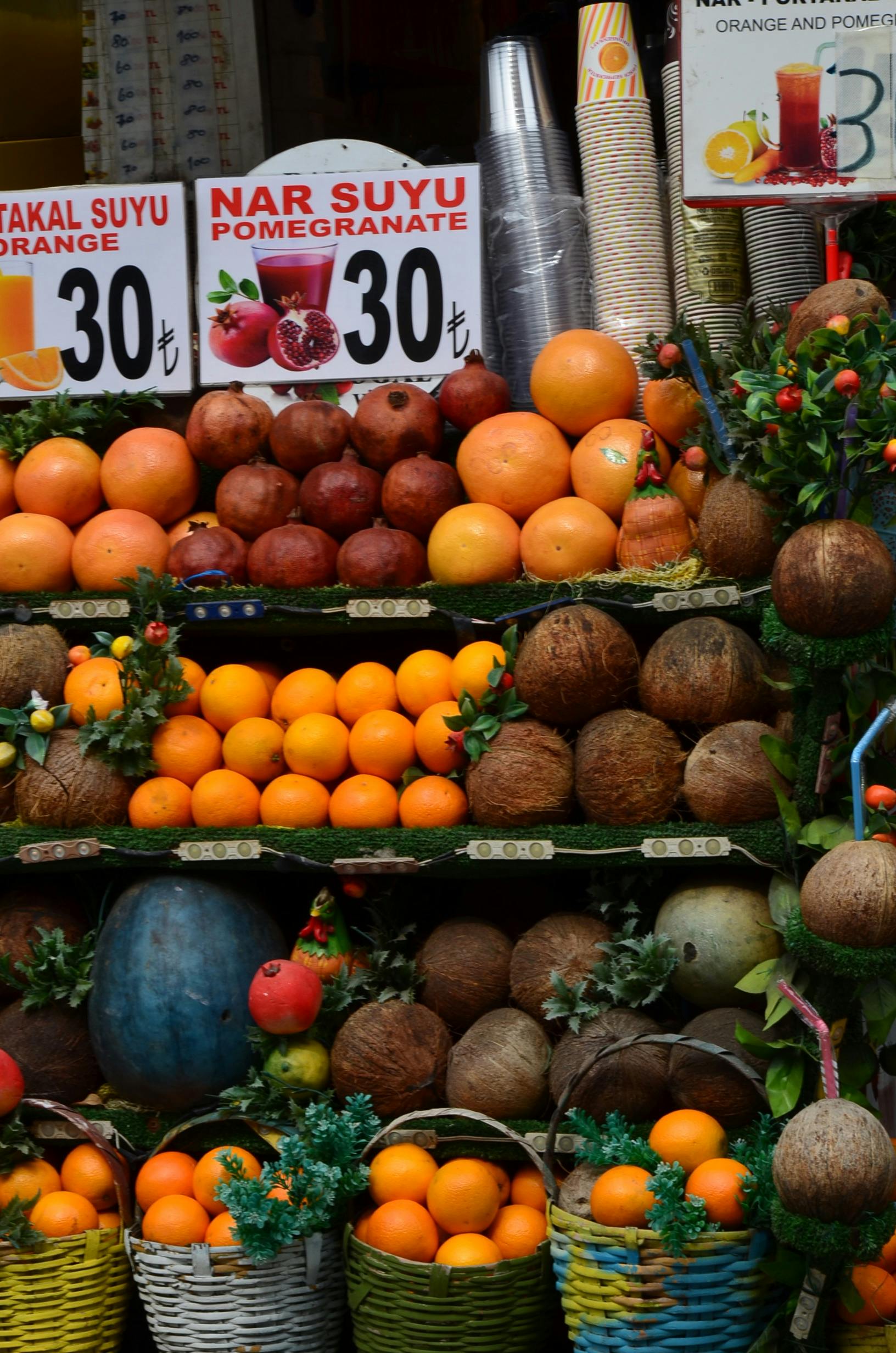 Colorful fruit stall with oranges, pomegranates, and coconuts in a busy market setting.