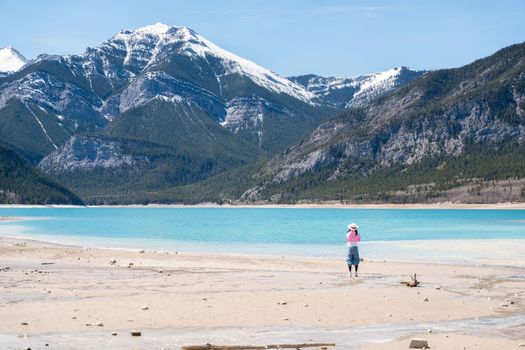 A lone woman stands at Barrier Lake, Kananaskis, with majestic mountains in the background.