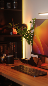 Cozy office desk with computer monitor, keyboard, and plants under warm lighting.