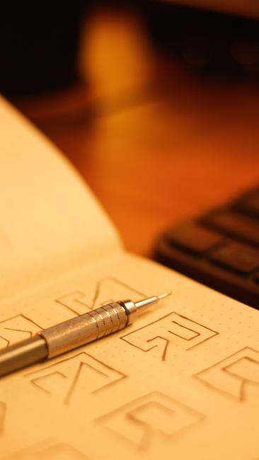 Metal pen resting on open notebook with geometric sketches, warm lighting.