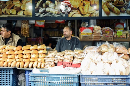 A man stands behind a counter with bread and other items