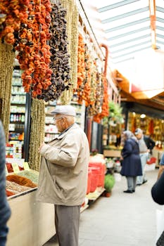 Elderly man in jacket browsing spices at a bustling indoor market with dried vegetables.