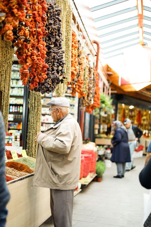 Free Elderly man in jacket browsing spices at a bustling indoor market with dried vegetables. Stock Photo