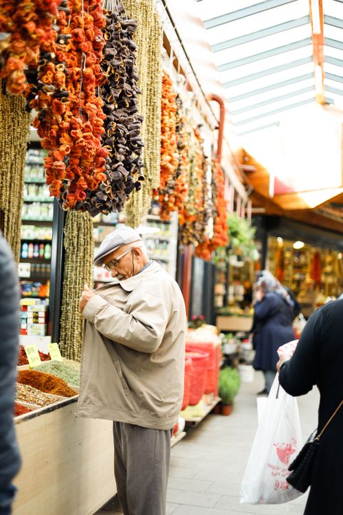 Free Senior man exploring a colorful market with spices and dried herbs hanging overhead. Stock Photo