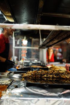 A street food vendor cooks grilled dishes at a bustling night market stand.