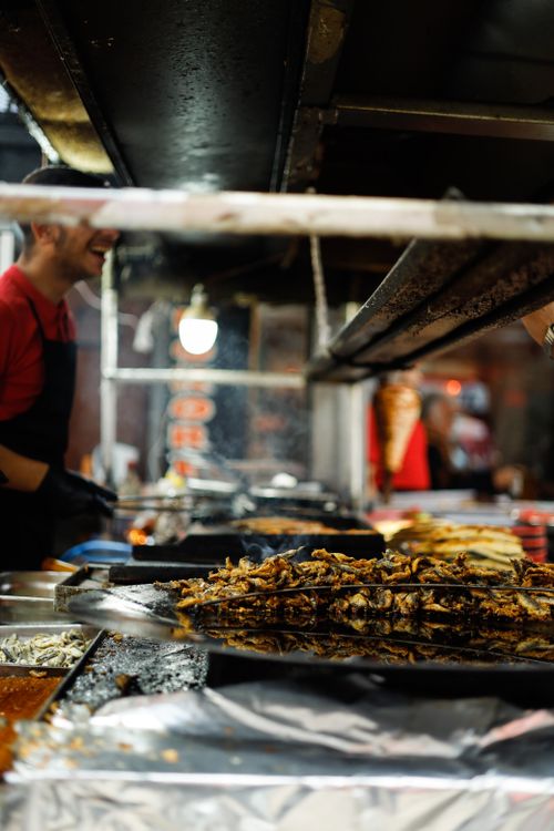 Free A street food vendor cooks grilled dishes at a bustling night market stand. Stock Photo