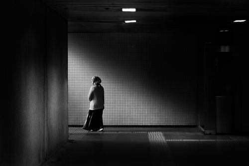 Free A solitary woman walks in a dim urban tunnel in black and white. Stock Photo