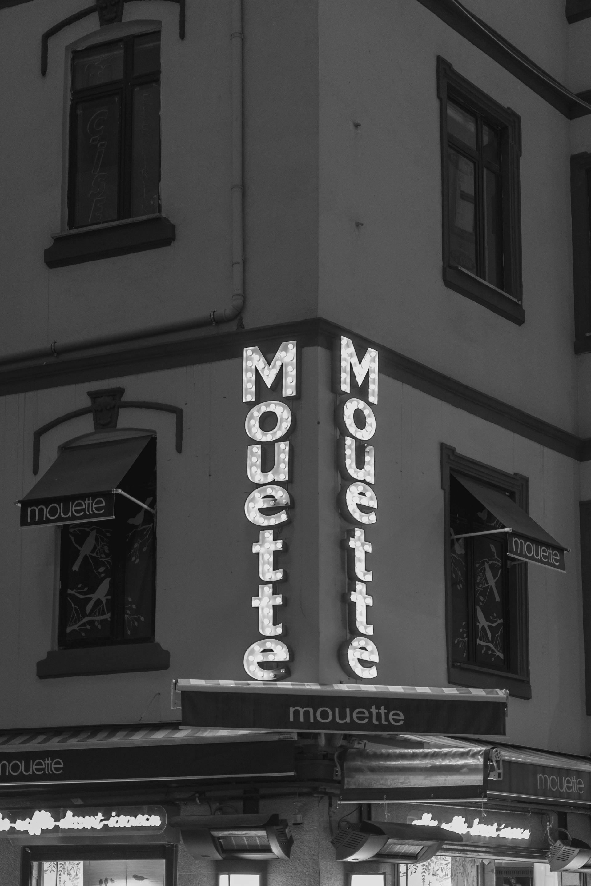 Free Monochrome image of a corner restaurant with illuminated sign 'Mouette' in urban setting. Stock Photo