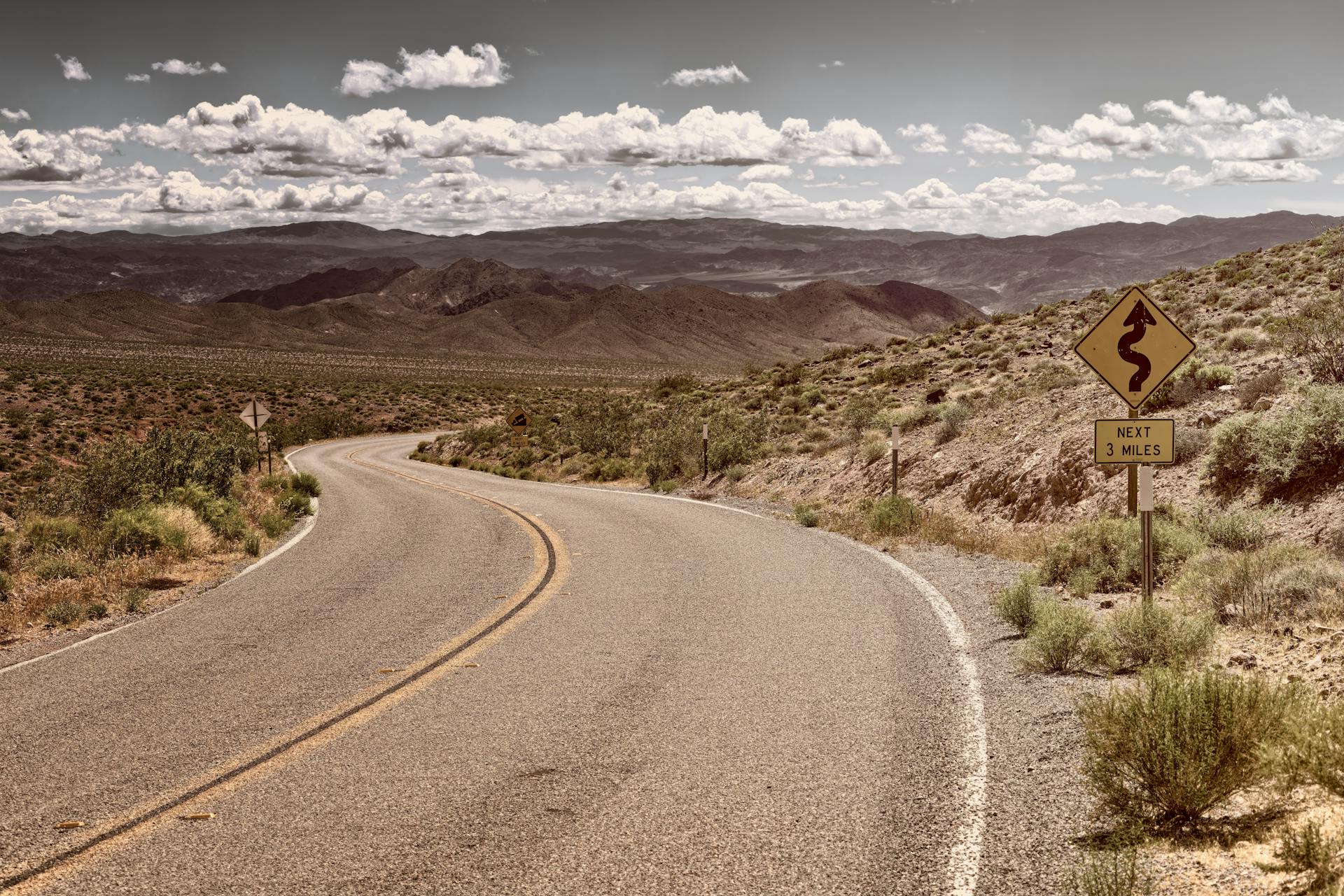 Curved desert road in arid landscape with mountains and clear sky