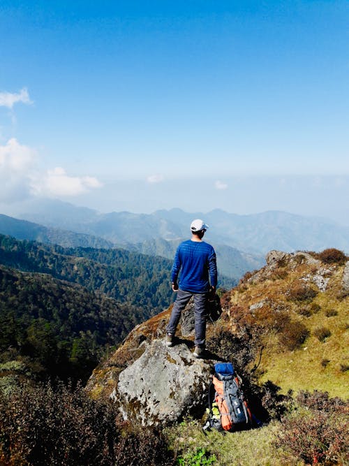 Free Man With White Cap and Blue Long-sleeved Top Standing on Rock Stock Photo