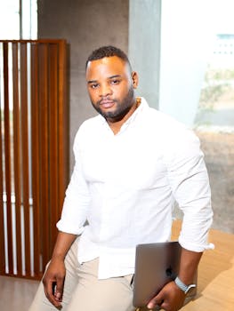 Confident man in white shirt holding laptop in a well-lit, modern indoor setting.