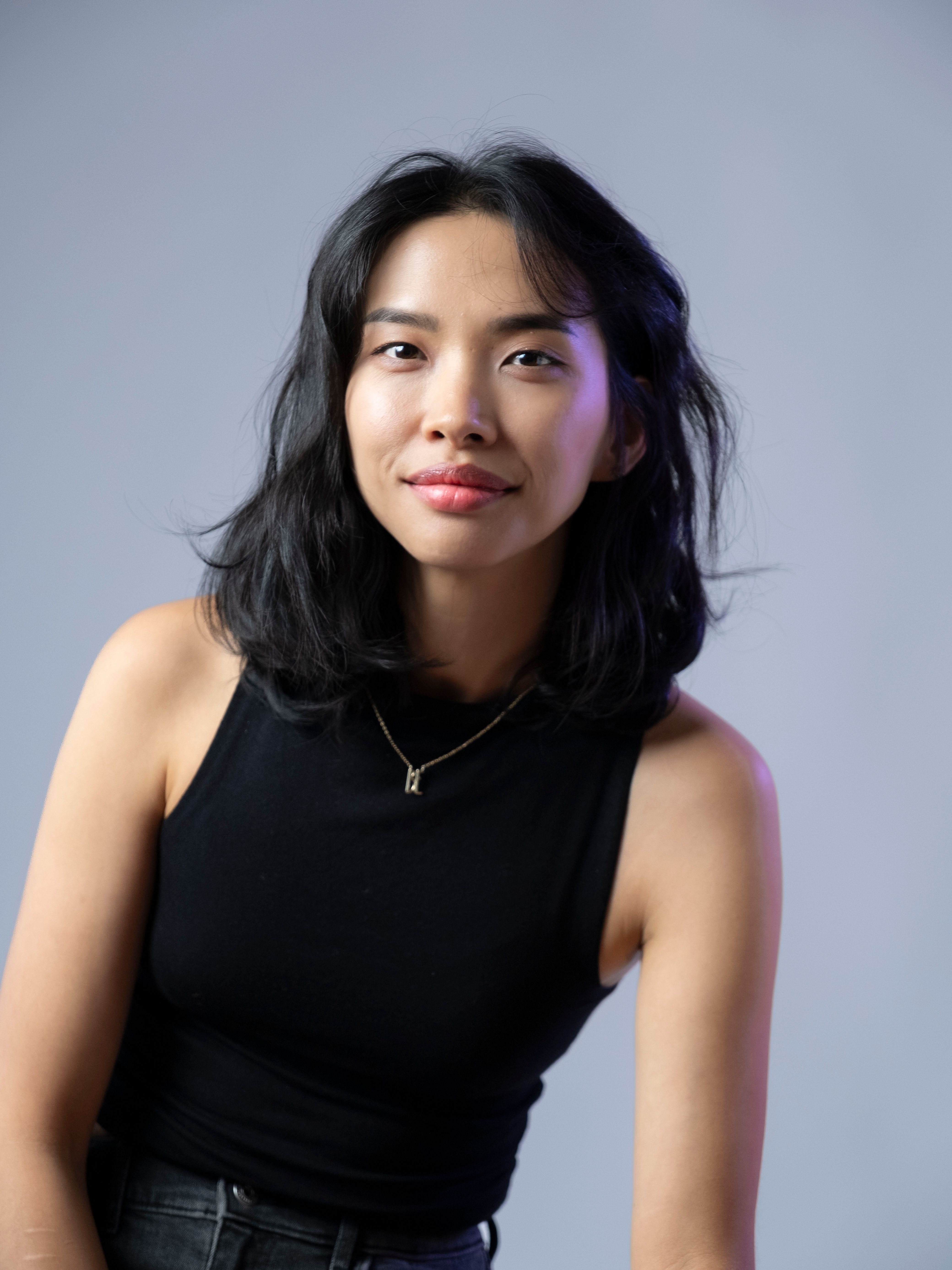 Fashionable Asian woman in black tank top smiling during studio photoshoot.