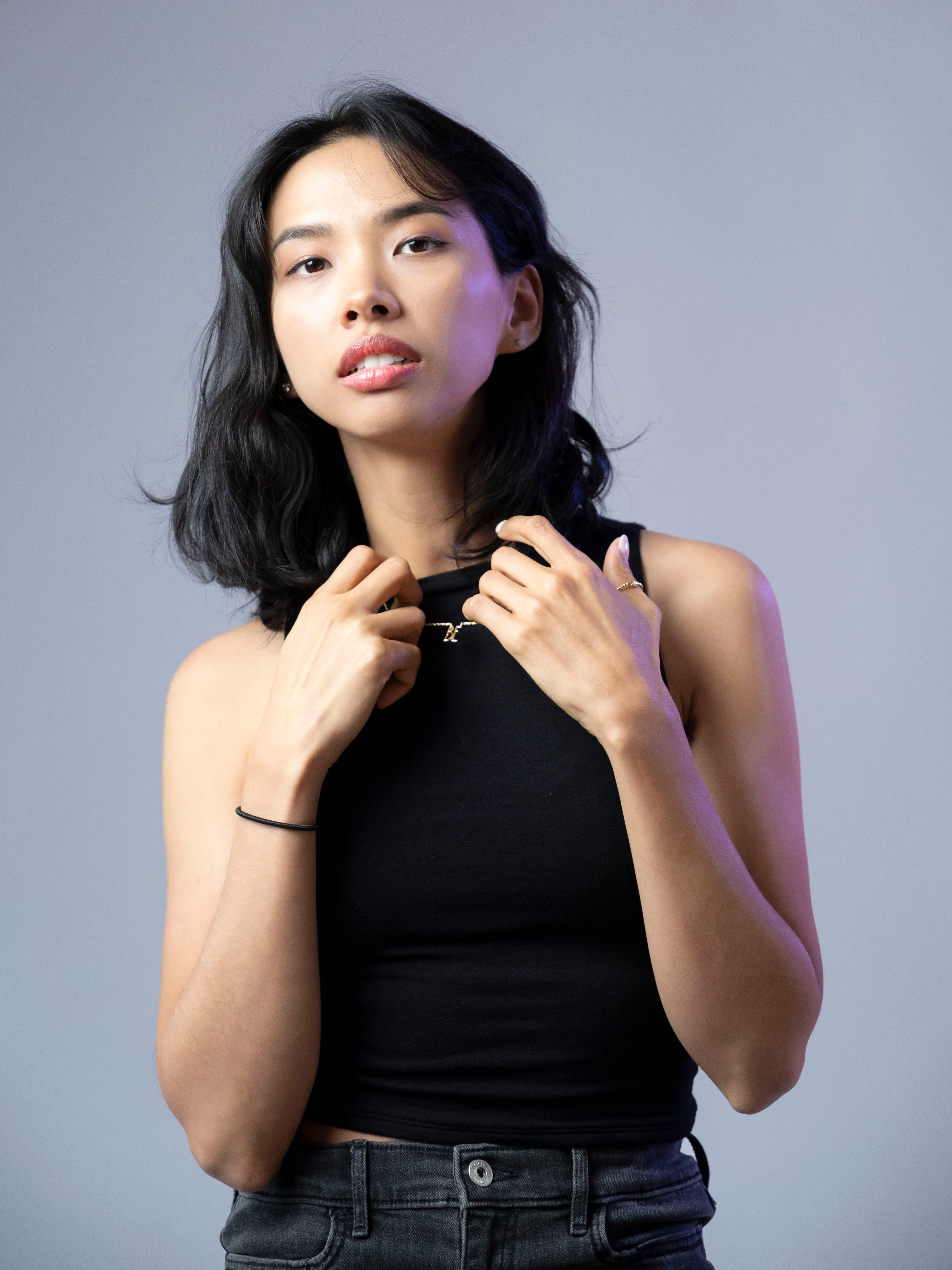 Studio portrait of an Asian woman in a black tank top with a gray background.