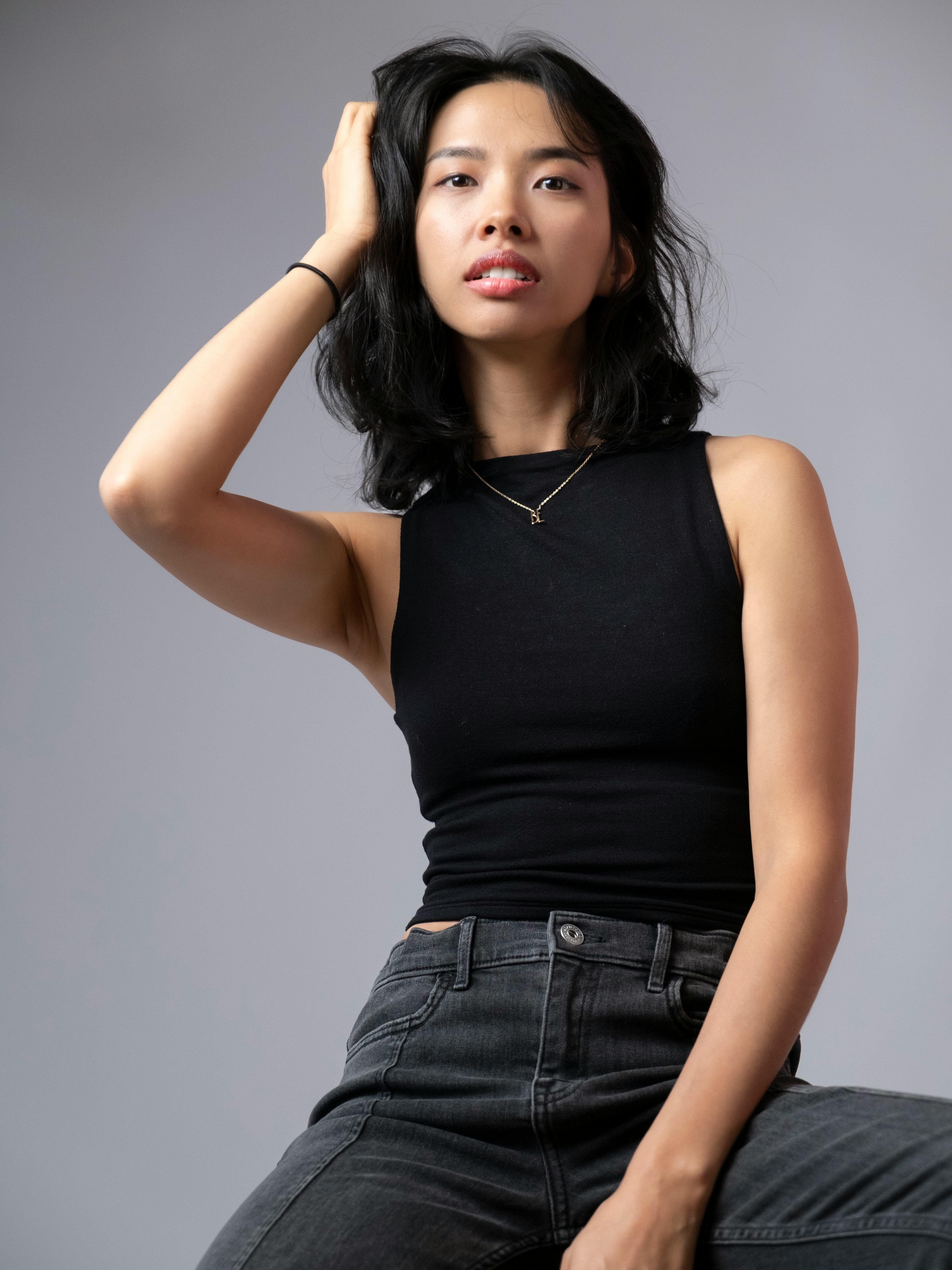 Stylish woman in a black tank top posing confidently with a gray studio background.