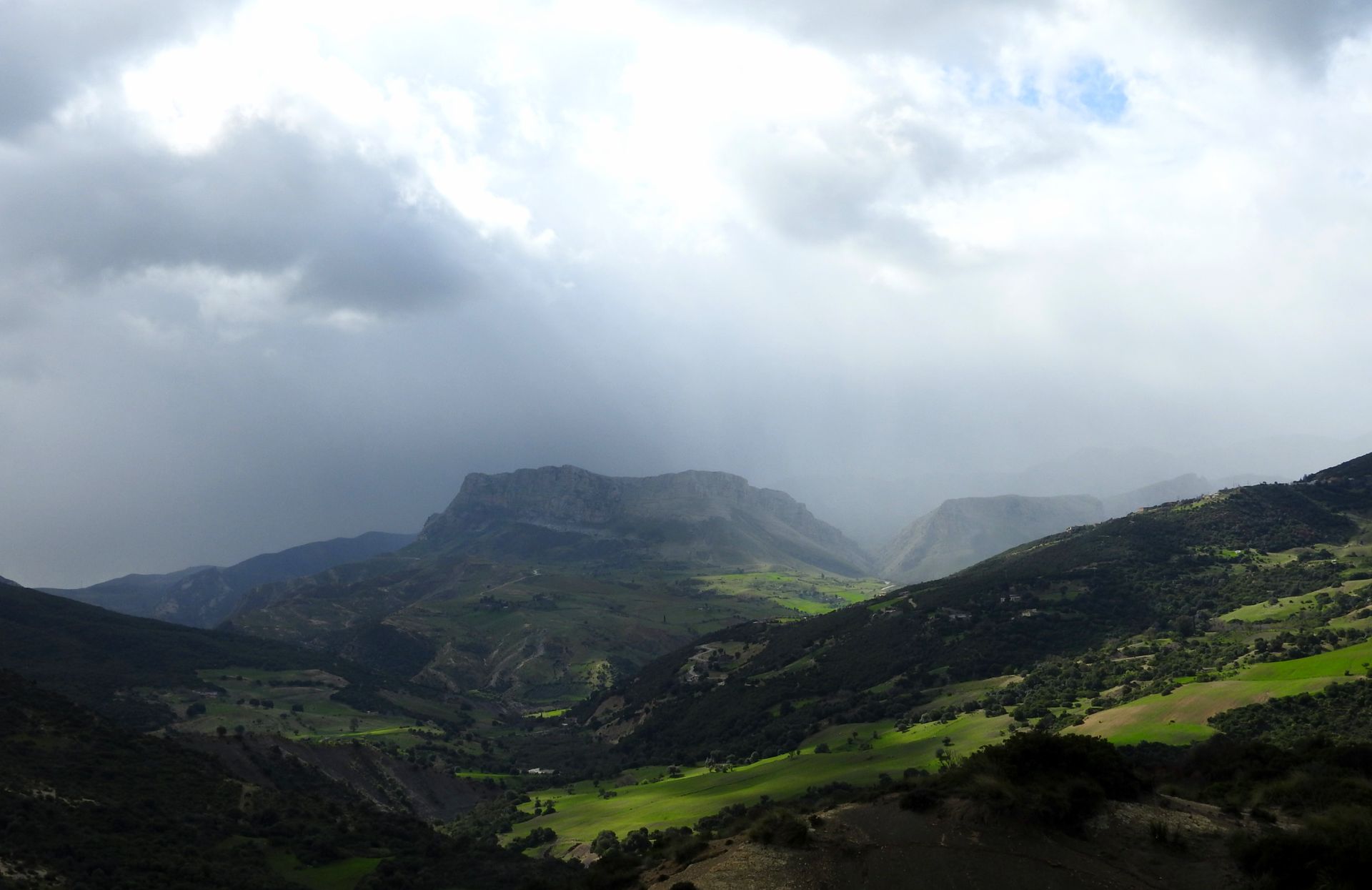 Breathtaking view of Algerian mountains with green valleys under a dramatic cloudy sky.