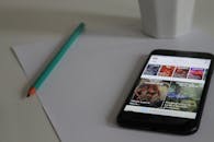 在工作空间中，智能手机显示新闻，旁边是桌子上的铅笔和纸，展示了现代技术