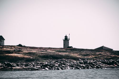 Free A picturesque lighthouse standing on a rocky coastline under a clear sky. Stock Photo