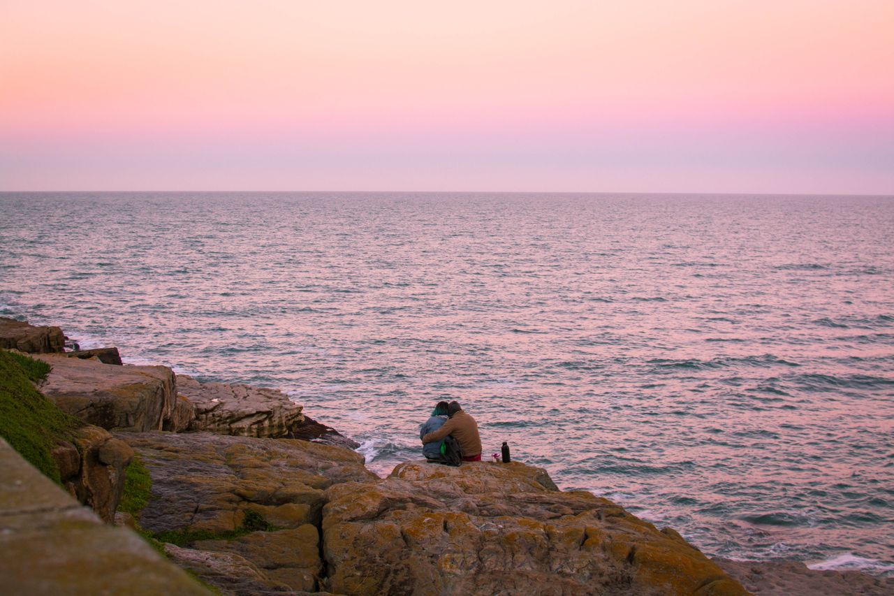 a couple shares a tender moment on rocky shores during a serene twilig